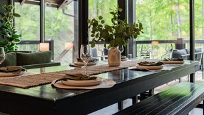 A dining table set with plates, glasses, and a vase, in a room with large windows and a sloped ceiling. - Indoor Private Pool, Sleeps 12, In Gatlinburg (Gatlinburg)