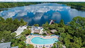 Una località turistica con piscina, sdraio e un molo che si estende in un lago.