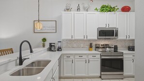 Una cucina moderna con mobili bianchi, elettrodomestici in acciaio inossidabile, un lavello doppio e una lampada a sospensione.