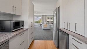 A modern kitchen with stainless steel appliances, white cabinetry, and a view to a balcony with a sofa. - Alpine Lakeview Residence (Queenstown)