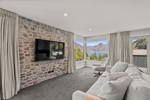 Un salon moderne avec un mur en pierre, un téléviseur à écran plat, un canapé gris et une vue sur les montagnes.