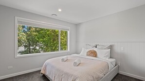A bedroom with a large window, a bed with a checkered bedspread, and a wall-mounted light fixture. - Alpine Lakeview Residence (Queenstown)