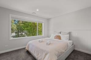 Ein Schlafzimmer mit großem Fenster, einem Bett mit kariertem Überwurf und einer Wandleuchte.
