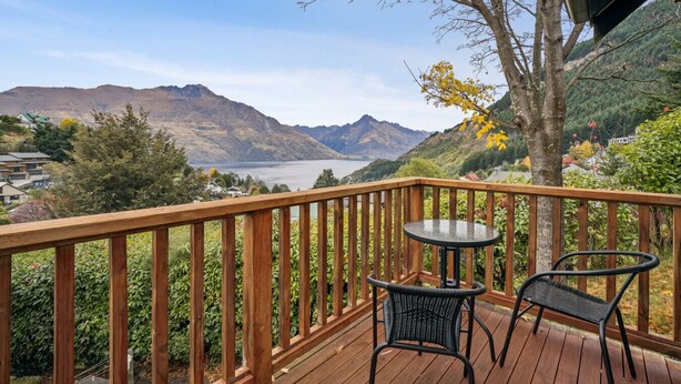 Eine Holzterrasse mit zwei Korbstühlen und einem Tisch, mit Blick auf einen See und Berge.