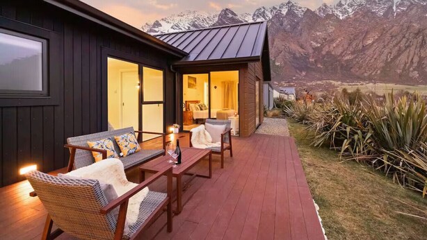 Un rincón exterior acogedor con mobiliario de mimbre y una mesa de madera, con vistas a un paisaje montañoso.