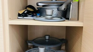 Ein Küchenschrank mit Kochgeschirr, darunter Töpfe und eine Reibe.