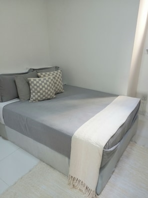 Ein Bett mit einer grau-weißen Tagesdecke, einem karierten Kopfkissen und einer weißen Decke.