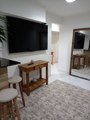Ein modernes Wohnzimmer mit Flachbildfernseher, Holzmöbeln, einem großen Spiegel und einem Blumentopf.