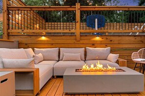 An outdoor seating area with a fire feature, wooden deck, and a blue chair. - Sylvans Escape - Pool, Hot Tub, Games, Sleeps 12, 10mins from World Cup Stadium (Atlanta)