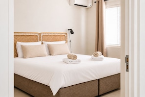 Ein ordentlich gemachtes Bett mit weißen Leinen, eine schwarze Stehlampe und zwei zusammengerollte Handtücher.