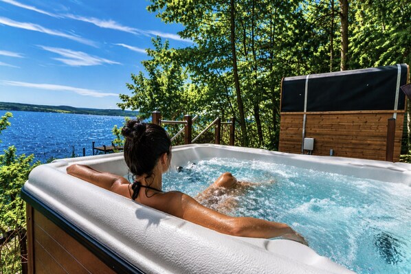 A hot tub with a view of a lake, surrounded by trees.