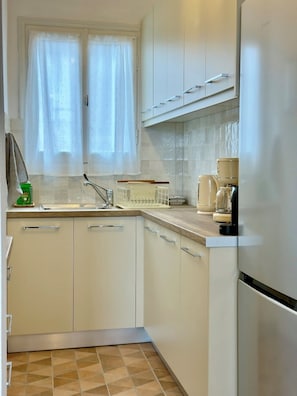 A kitchen with white cabinets, a window with sheer curtains, a coffee maker, and a sink.