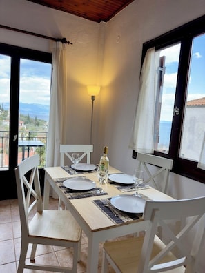 A dining area with a table set for two, a bottle of wine, and a view of the sea.