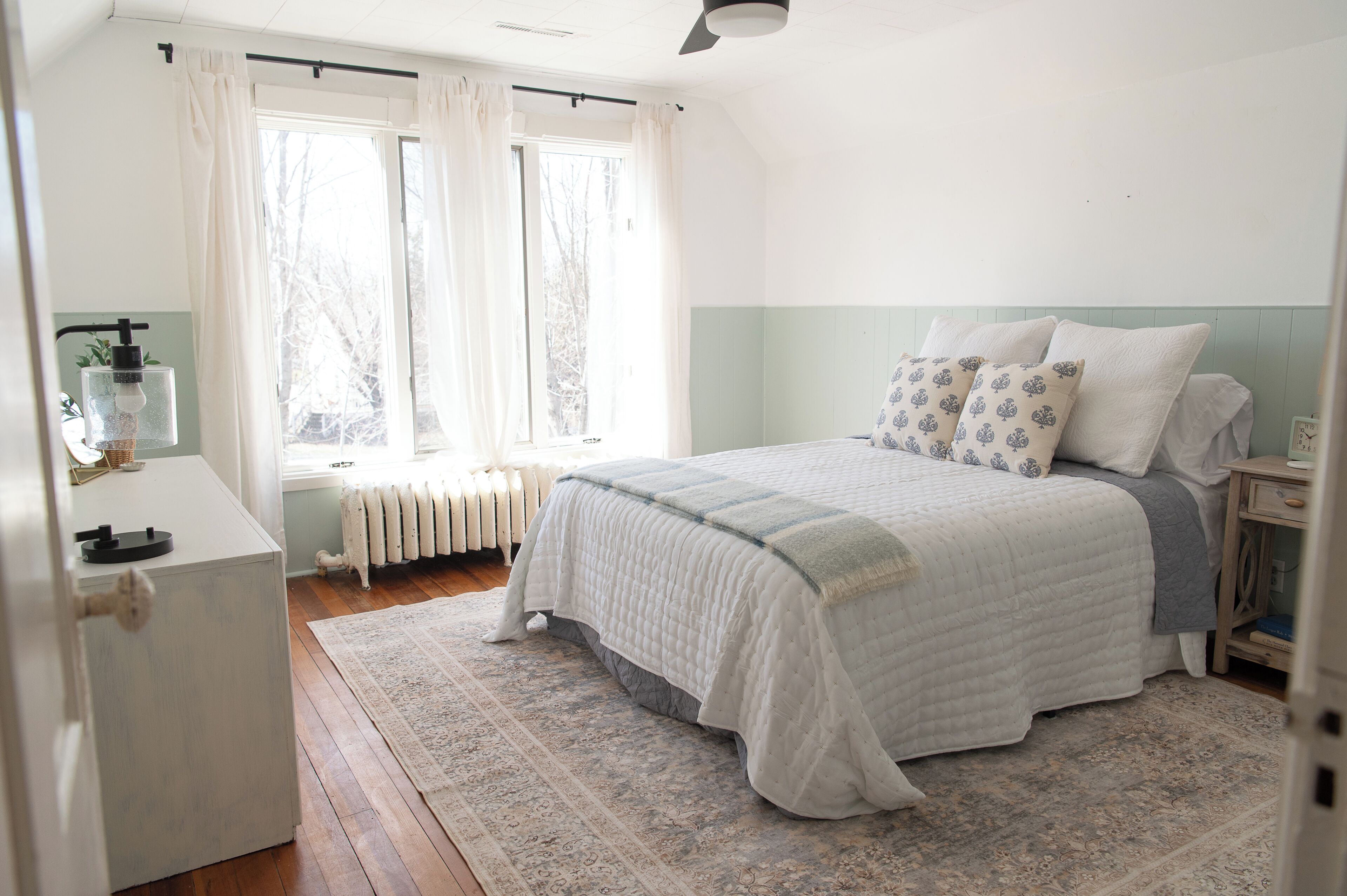 A bedroom with a bed, a nightstand, a dresser, a radiator, and a window with curtains.