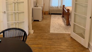 Ein Zimmer mit Holzboden, Heizkörper, Stuhl, Tisch und einer Tür mit Glasfeldern.