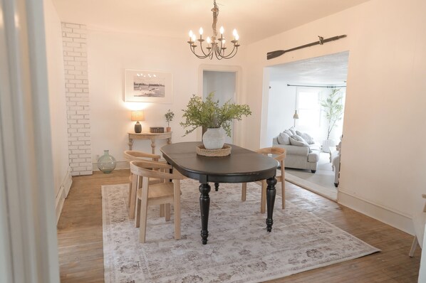 A dining area with a table, chairs, a chandelier, a vase with plants, and a framed picture on the wall.
