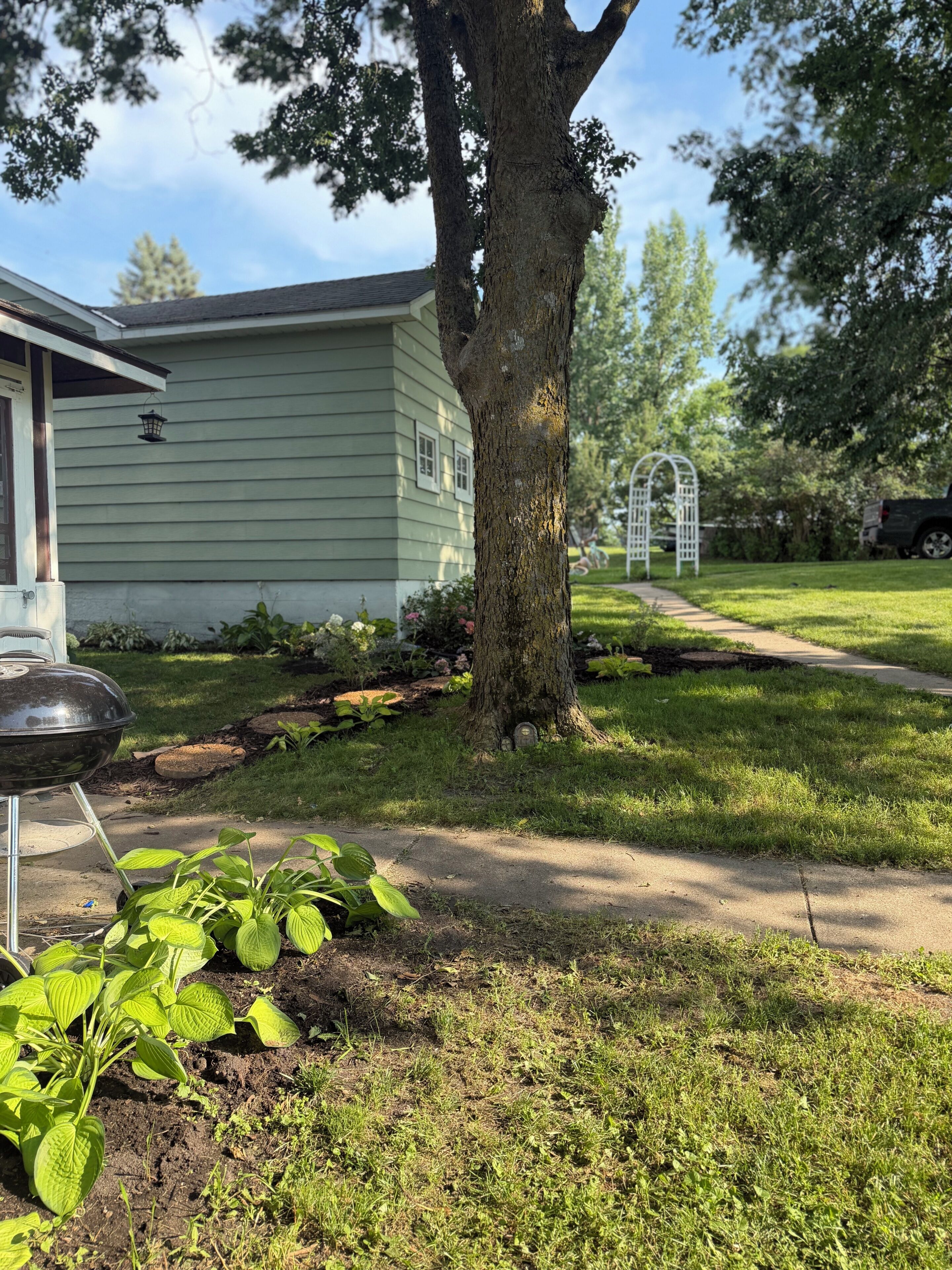 A residential property with a lawn, a tree, a barbecue grill, and a house with a light green exterior.