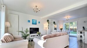 A modern living room with a TV, sofas, a dining area, and a view of the outdoors. - Tides & Trails - SAINT GILDAS DE RHUYS (SAINT GILDAS DE RHUYS)