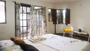 Una habitación con una cama, una silla, una mesita y un ventanal con cortinas.