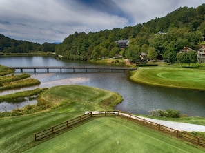 A golf course with a bridge, water bodies, and residential houses in the background.