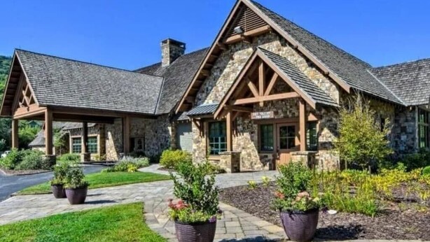 Un bâtiment en pierre avec un toit à deux versants et des poutres en bois, une entrée couverte et des plantes en pot au premier plan.