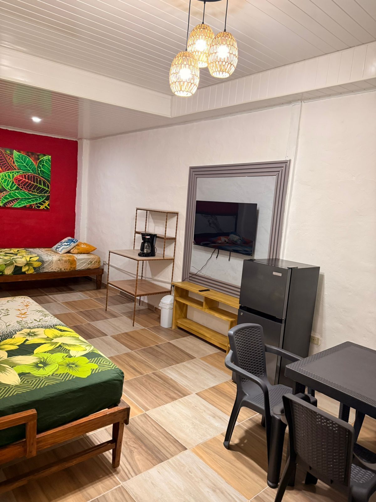 Una habitación con cama, escritorio, silla, televisor y estante con cafetera.