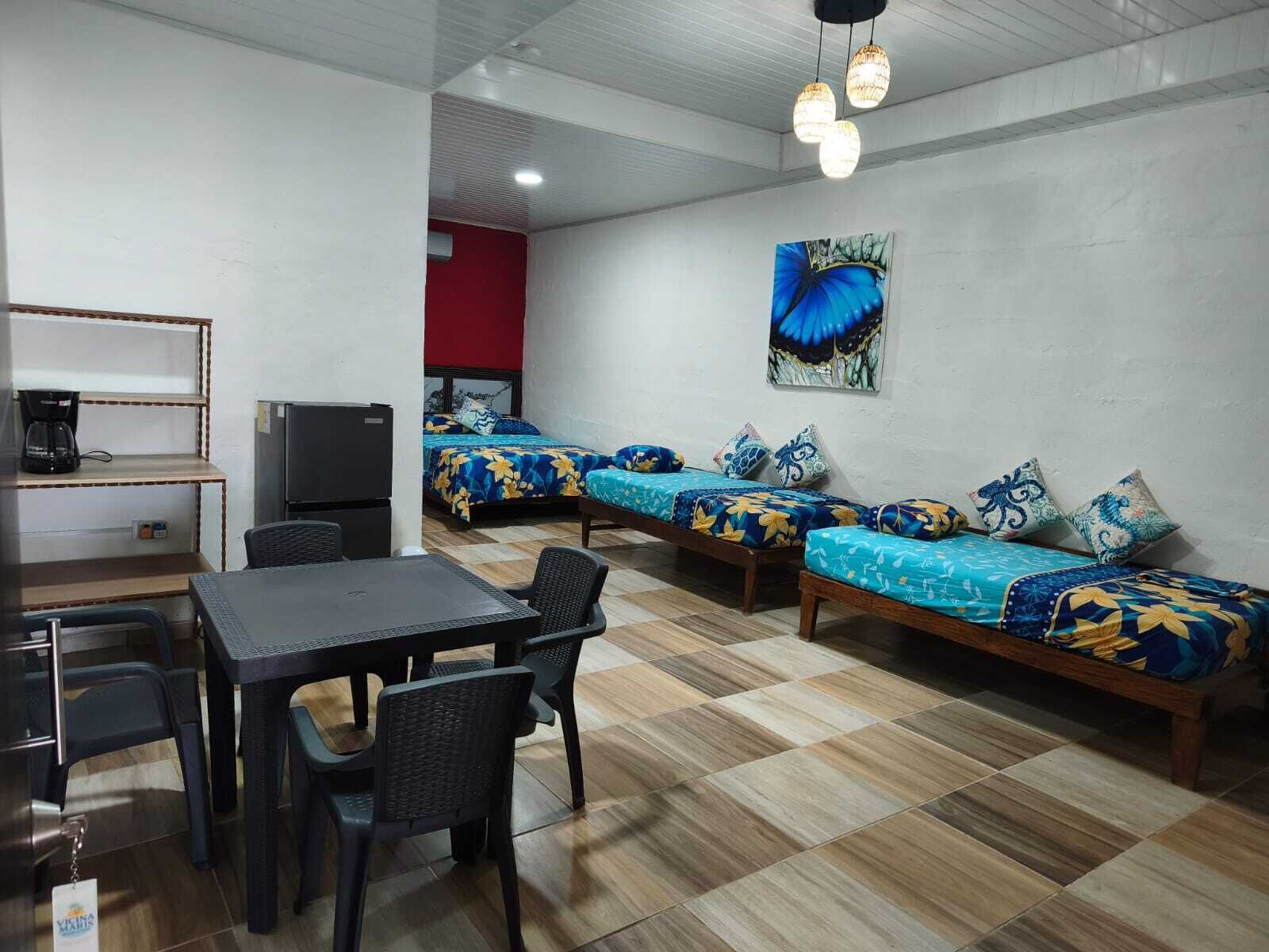 A room with a dining table, chairs, a TV, and two beds with floral bedding.
