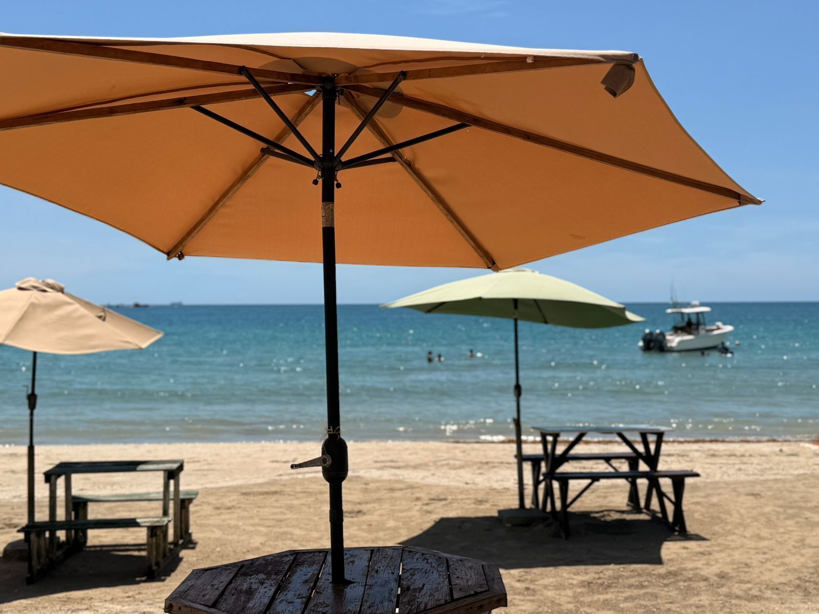 A beach with a large umbrella, a table, and a boat in the background.