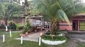 A building with a covered entrance, a palm tree, and a garden area.