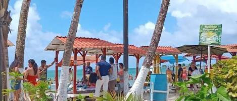 A beachside area with palm trees, a covered seating area, and a signboard.