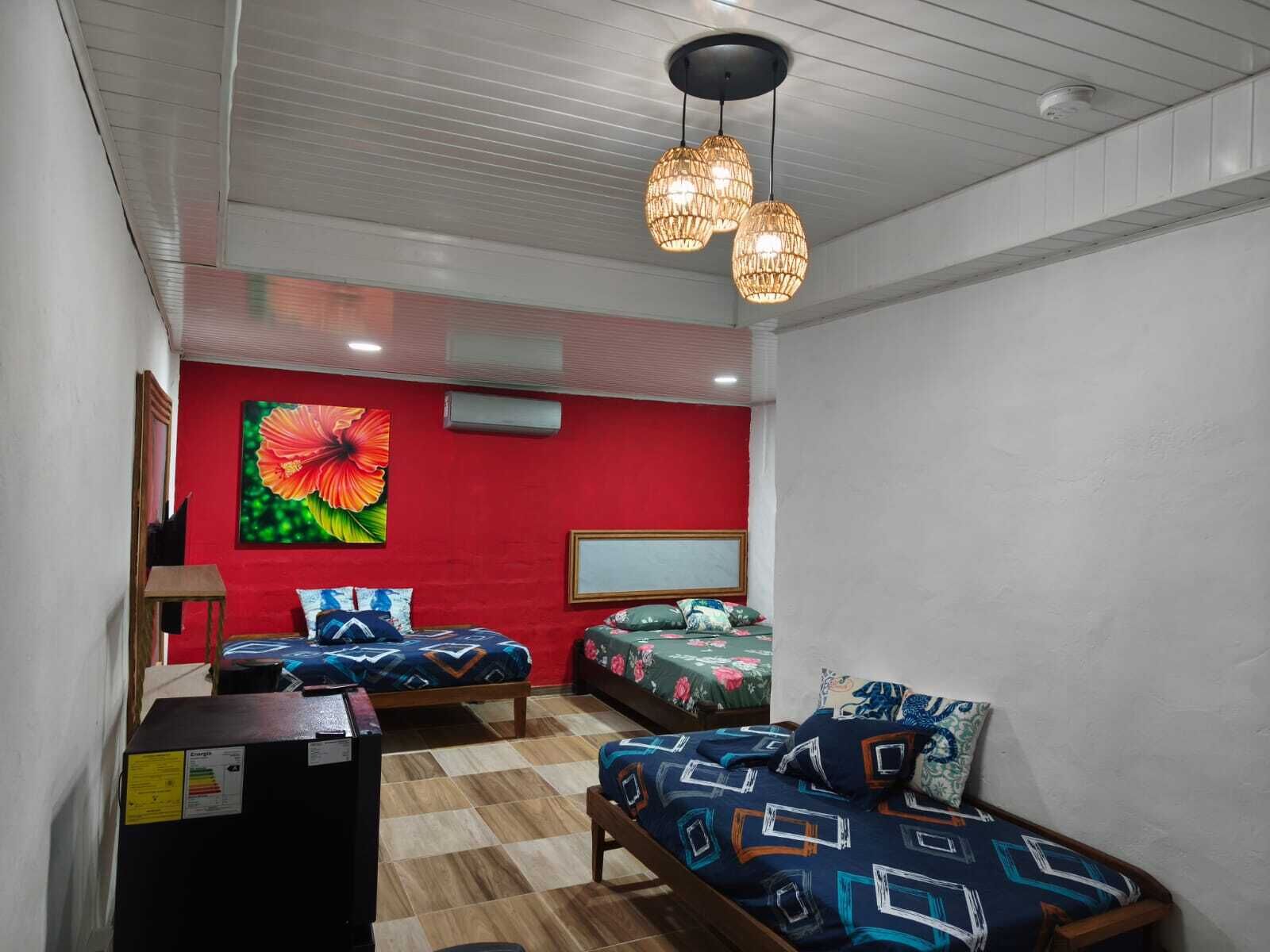 A bedroom with two beds, a red accent wall, and a large floral painting.
