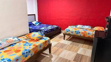 Una habitación con tres camas de madera, cada una con ropa de cama floral de colores, una pared roja y suelo de baldosas.