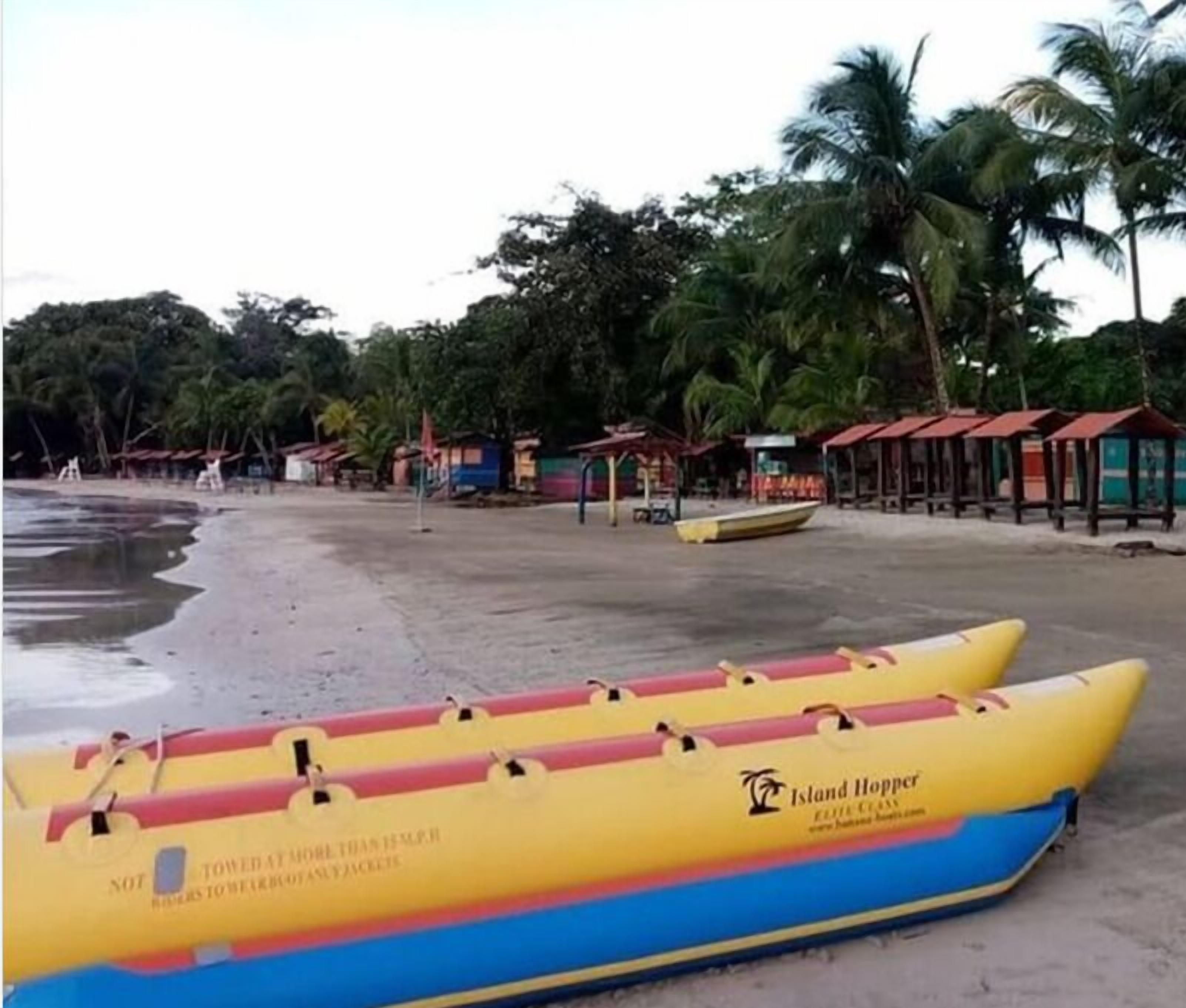 A beach with two yellow and blue inflatable boats labeled 'Island Hopper' and a row of small beach huts.