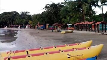 A beach with two yellow and blue inflatable boats labeled 'Island Hopper' and a row of small beach huts.
