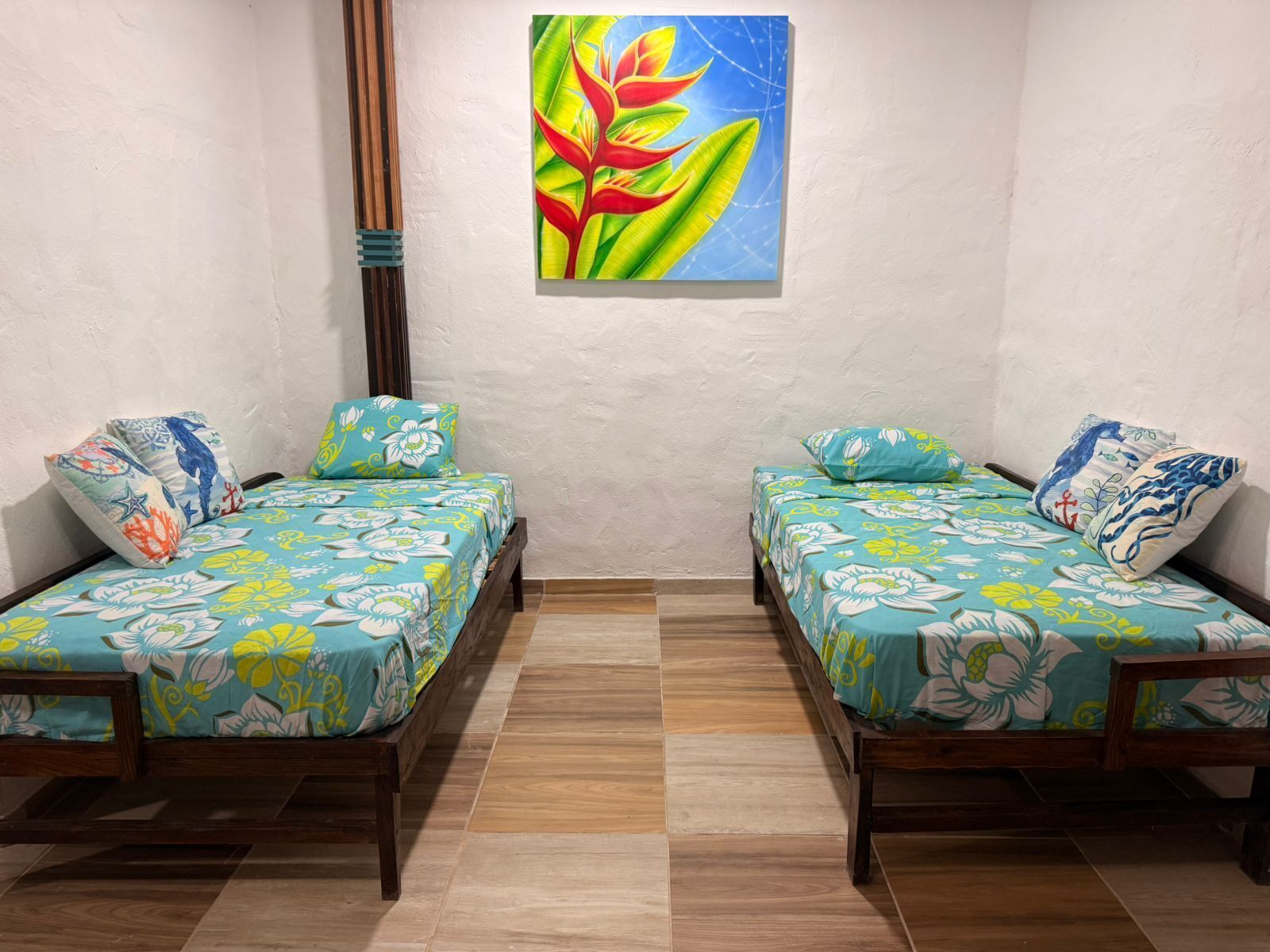 Una habitación con dos camas de madera, cada una con ropa de cama floral y almohadas a juego, un suelo de madera y un cuadro colgado en la pared con una planta.