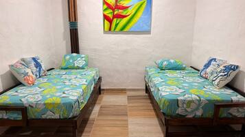 Una habitación con dos camas de madera, cada una con ropa de cama floral y almohadas a juego, un suelo de madera y un cuadro colgado en la pared con una planta.