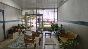 A spacious indoor area with a view of the beach, furnished with wicker chairs and tables, and decorated with potted plants. - Vicina Maris Beach Lodge (Maria Chiquita)