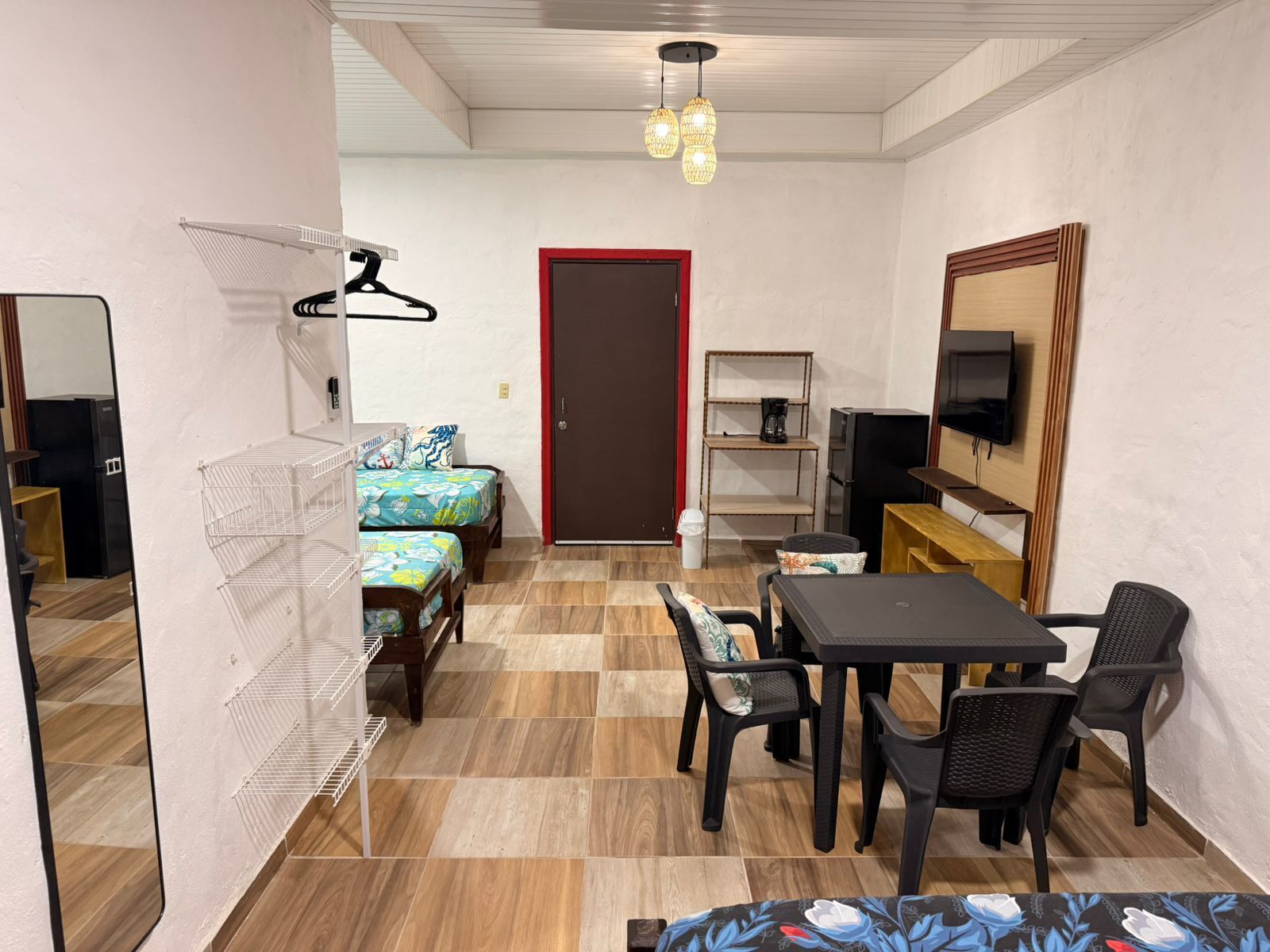 Quarto compacto com cama, mesa de jantar com cadeiras, televisão e uma pequena cozinha equipada.