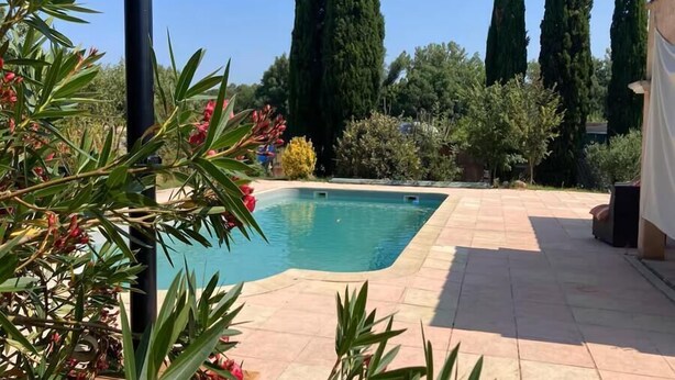 A swimming pool with a tiled deck, surrounded by tall cypress trees and various shrubs. - Villa La Graine de Vie with shared pool (LE THORONET)