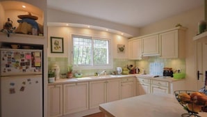 A kitchen with white cabinets, a window, a refrigerator, and a sink. - Villa La Graine de Vie with shared pool (LE THORONET)
