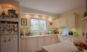 Una cocina con armarios blancos, un ventanal, un refrigerador y un lavamanos.
