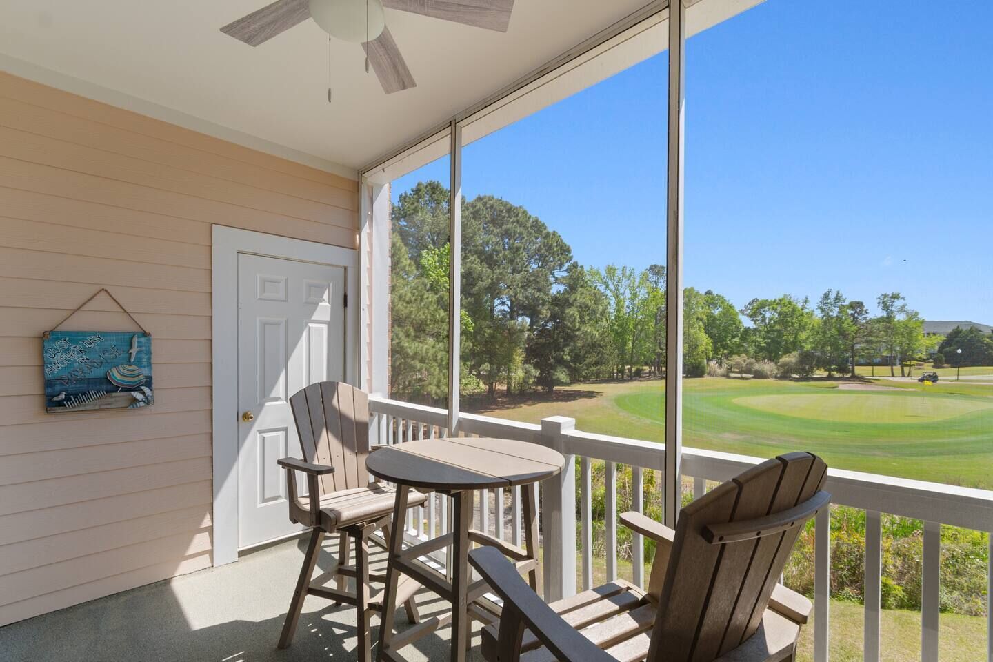 A porch with a table and chairs, a door, and a view of a golf course.