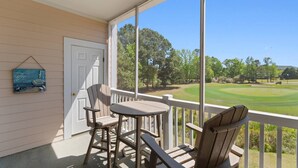 Une véranda avec une table et des chaises, une porte et une vue sur un terrain de golf.