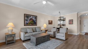 Un salon comprenant un canapé, des fauteuils, une table basse, un tapis, un ventilateur de plafond et des œuvres d’art accrochées aux murs.