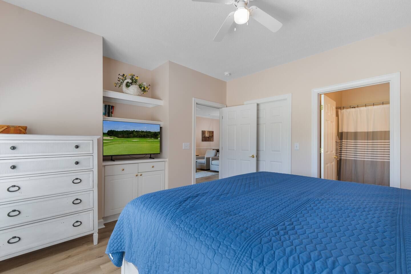 A bedroom with a bed, a dresser, a television, and a ceiling fan.
