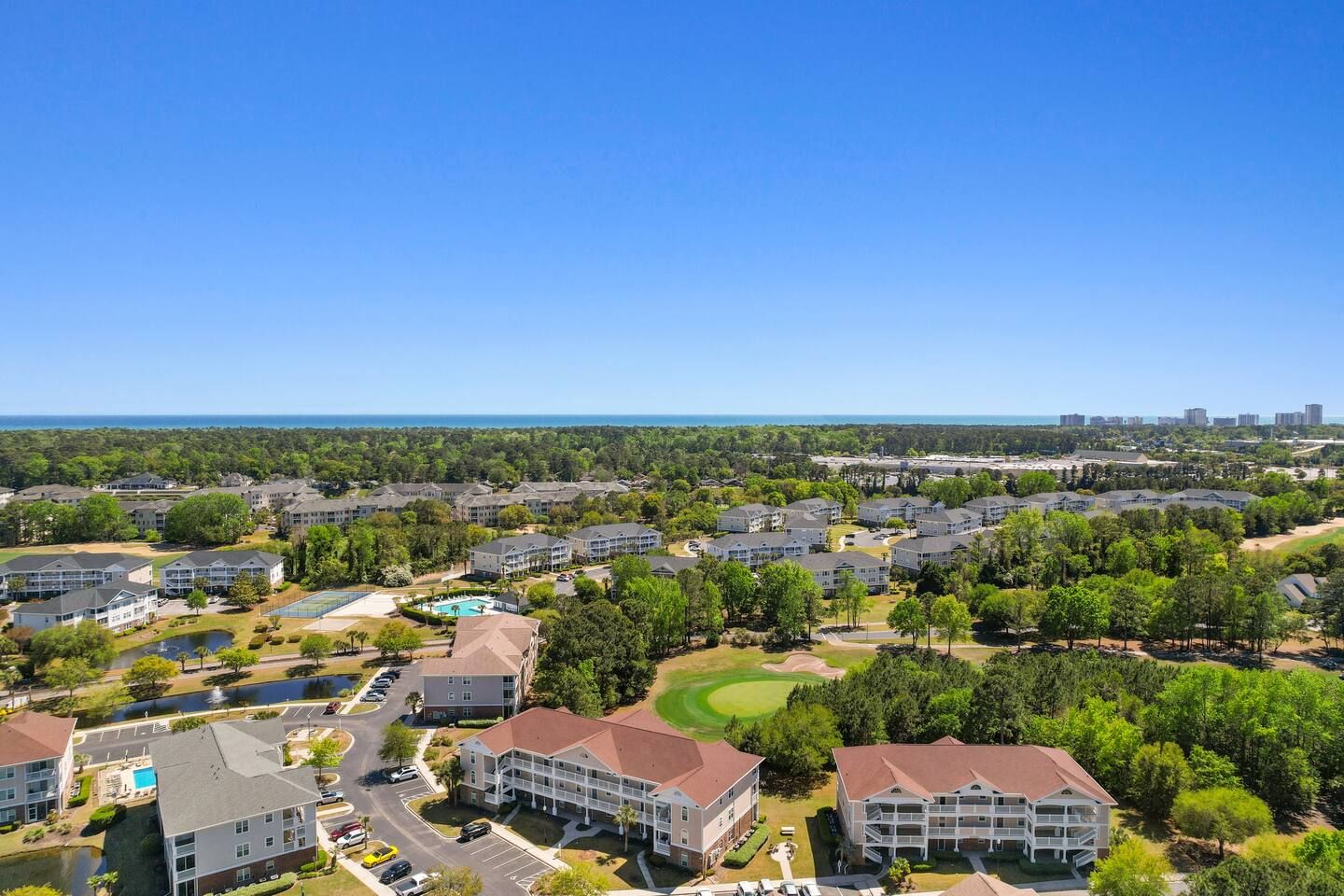 A residential area with multiple apartment buildings, a golf course, and a clear blue sky.