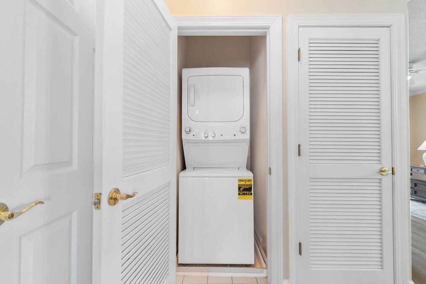 A compact laundry room with a washer and dryer, a door with a brass handle, and a white tiled floor.