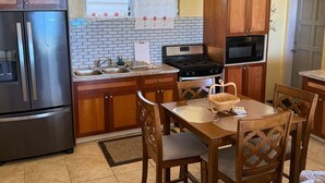 Una cocina con armarios de madera, un refrigerador de acero inoxidable, una estufa a gas, un microondas y una mesa de comedor con sillas.