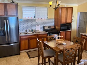 A kitchen with wooden cabinets, a stainless steel refrigerator, a gas stove, a microwave, and a dining table with chairs. - VI Cozy Comfy, Generator, beautiful view, close DT (Charlotte Amalie)