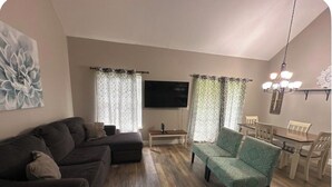 A living room with a sofa, a patterned armchair, a TV, and a dining area with chairs and a table. - Cozy 2-bedroom condo in perfect Branson with AC (Branson)